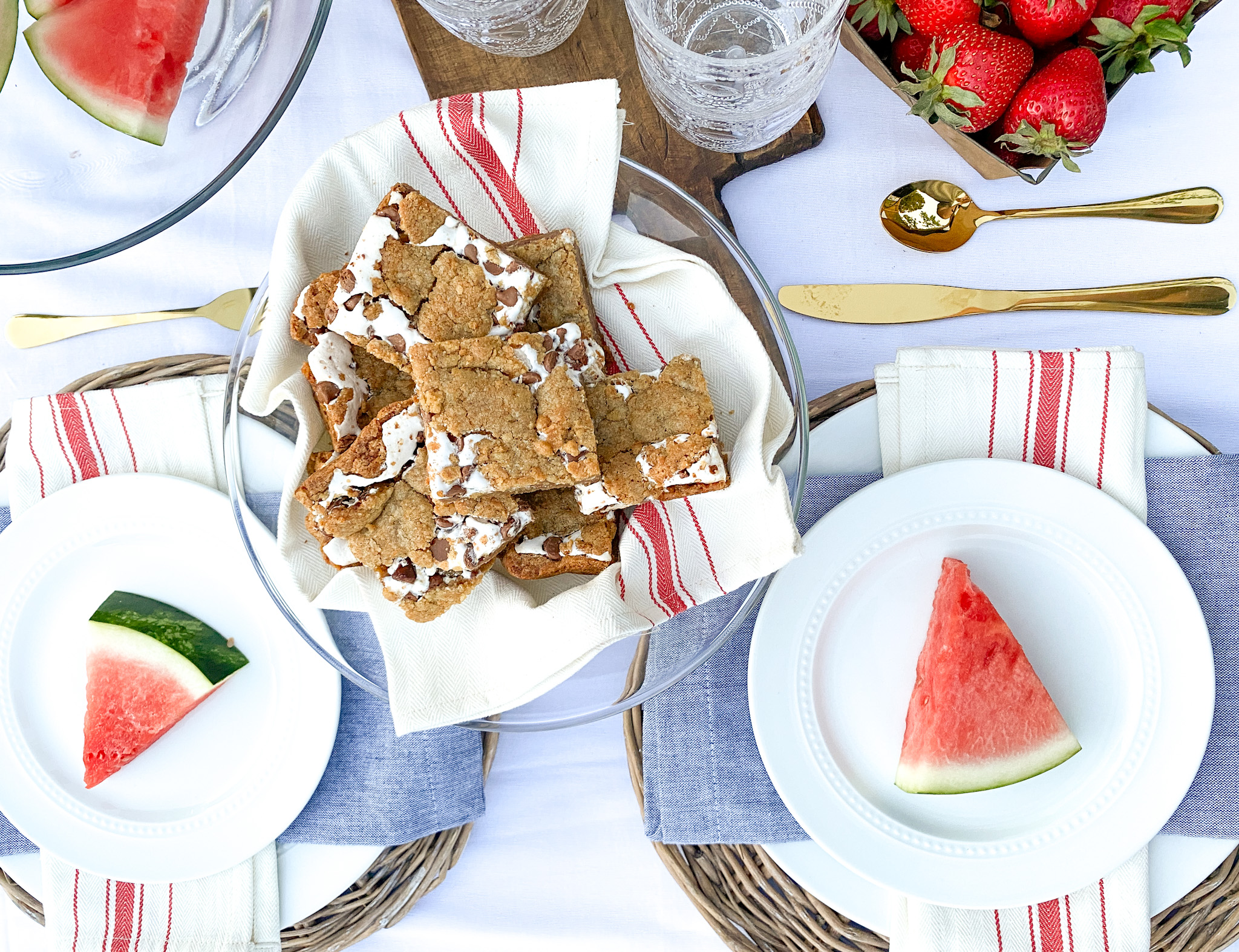 Overhead view of BBQ party table with a place of smores bars, basket of fresh strawberries, and slices of watermelon