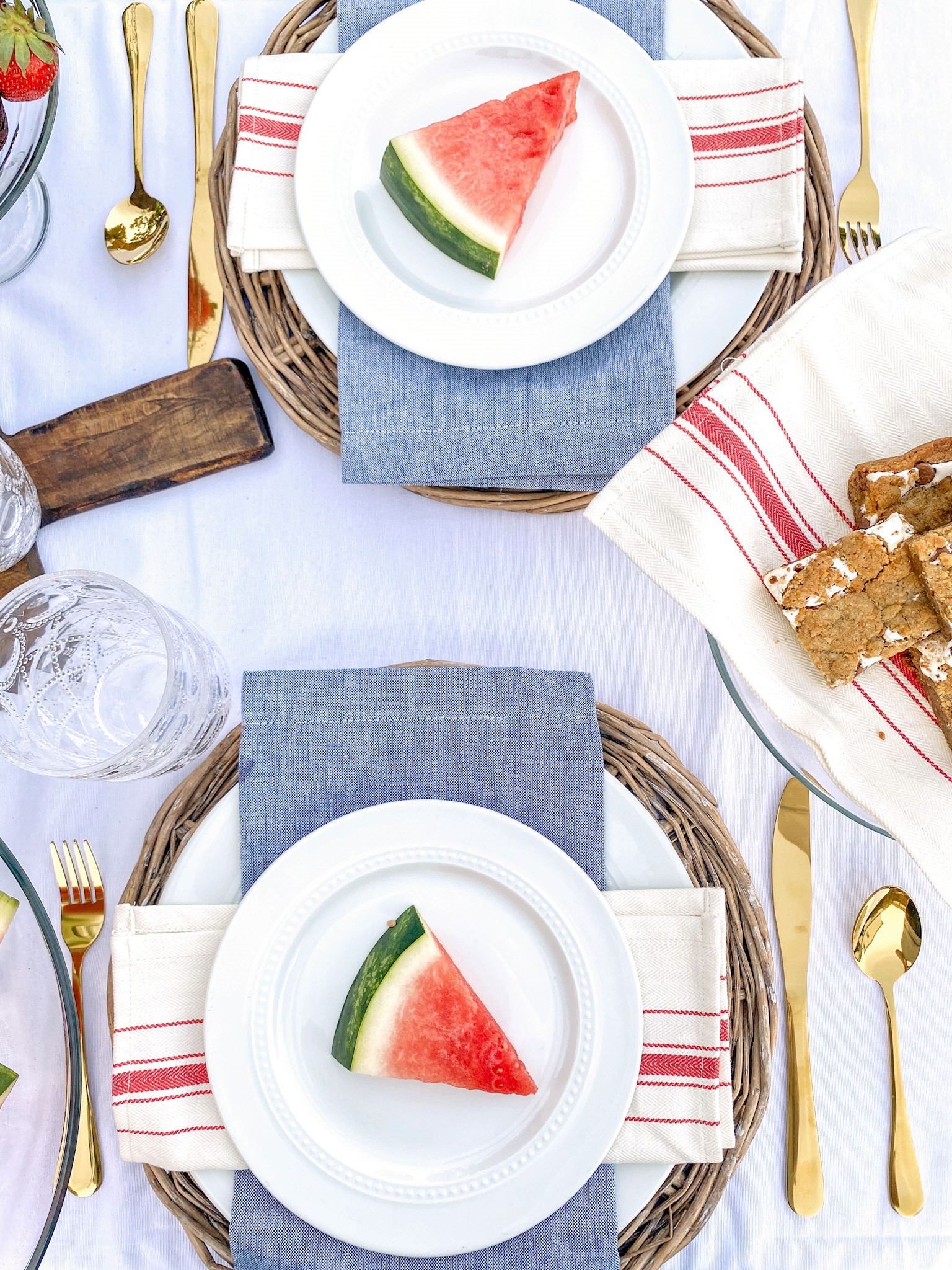 Overhead view of red, white, and blue patriotic table set for a backyard BBQ party for Memorial Day with slices of watermelon the plates and a plate of smores bars