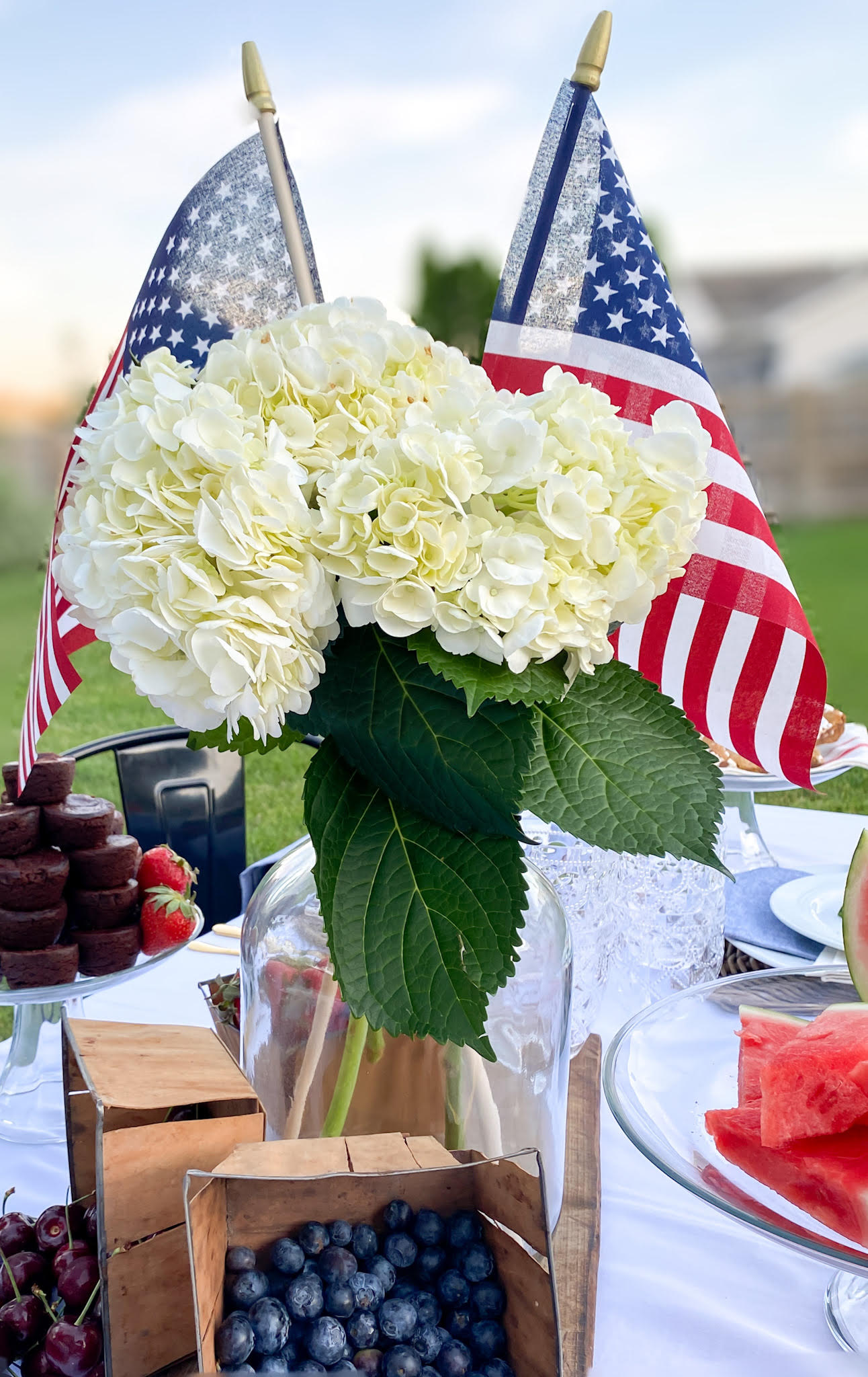 Close up view of patriotic summer ceterpiece for a BBQ party with a vase filled with white hydrangeas and American flags