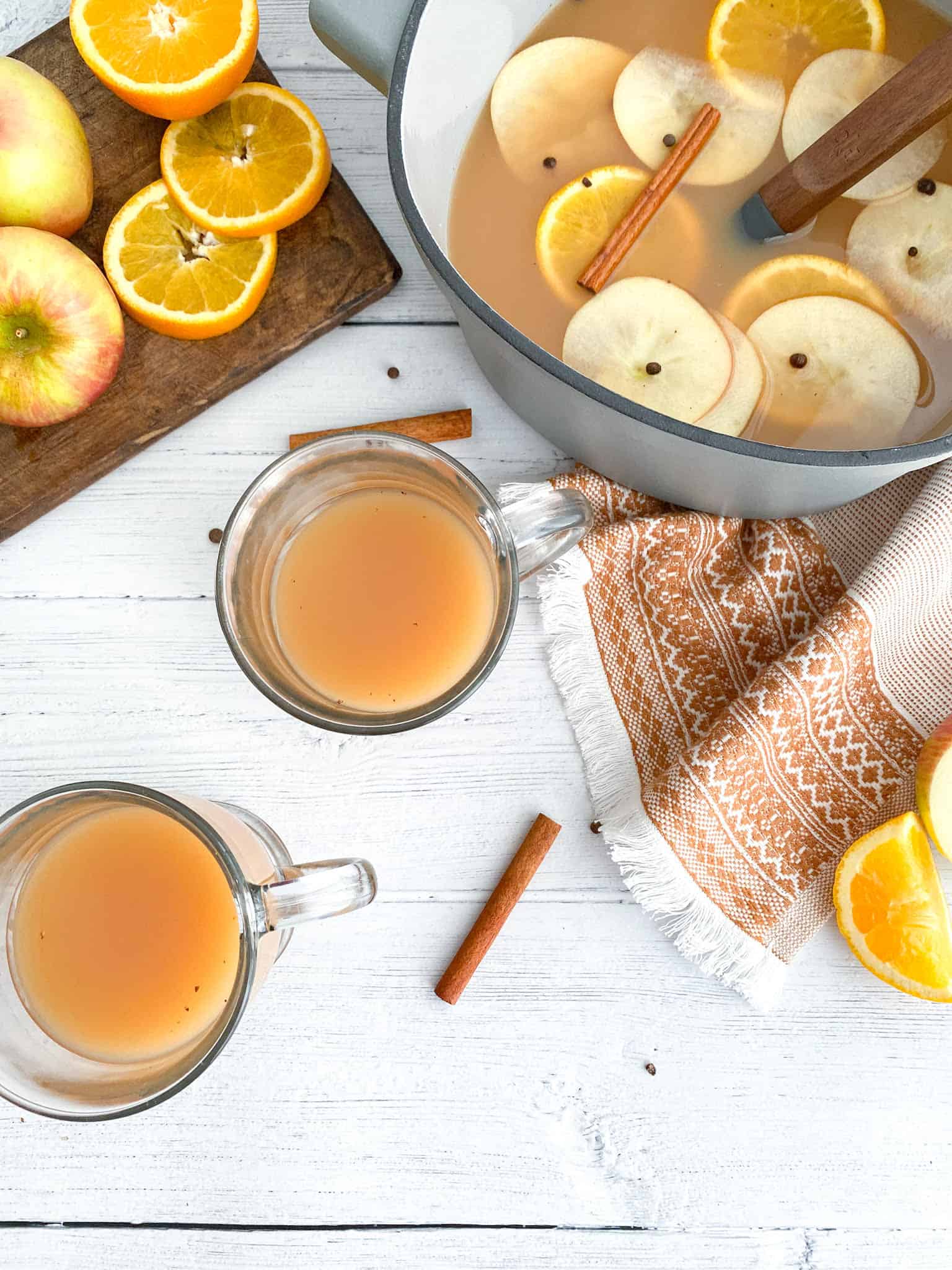 Homemade hot spiced apple cider ina large dutc oven with two galss mugs also filled with the cider