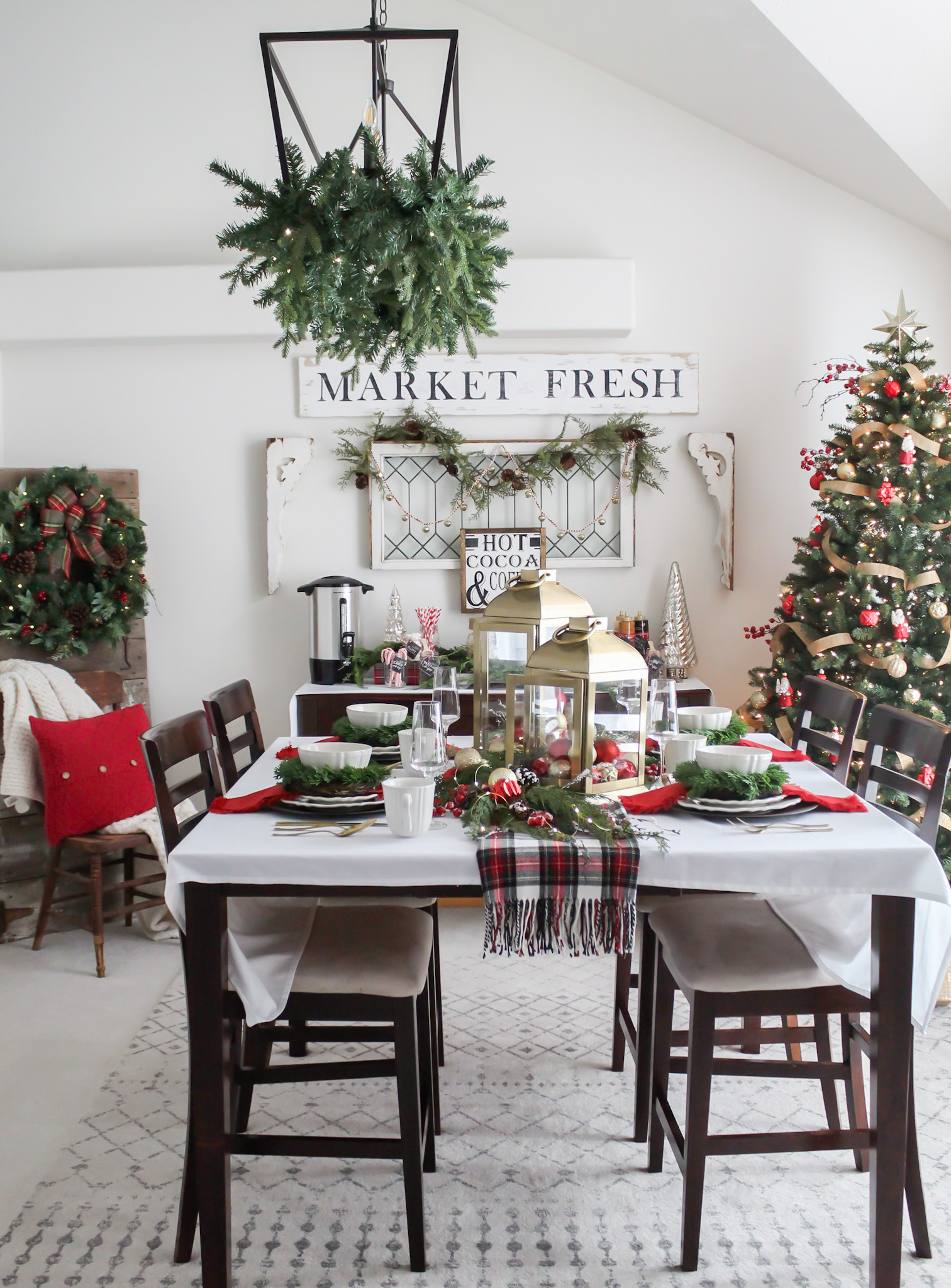 Dining room decorated for Christmas with red and gold decor, the table set for a holiday meal and a tree decorated in the corner