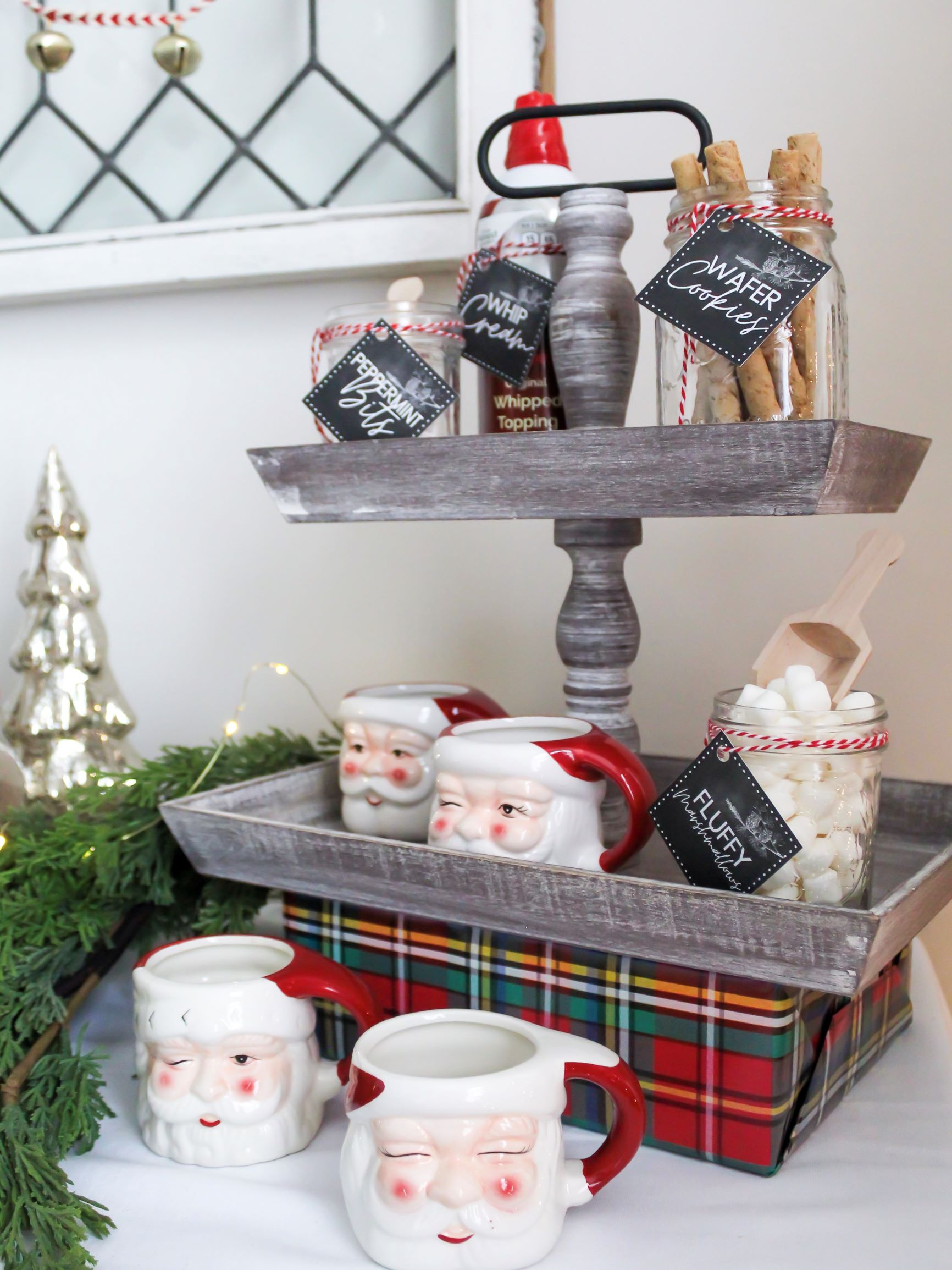 Tiered tray on a Christmas hot cocoa bar with toppings and Santa cofee mugs