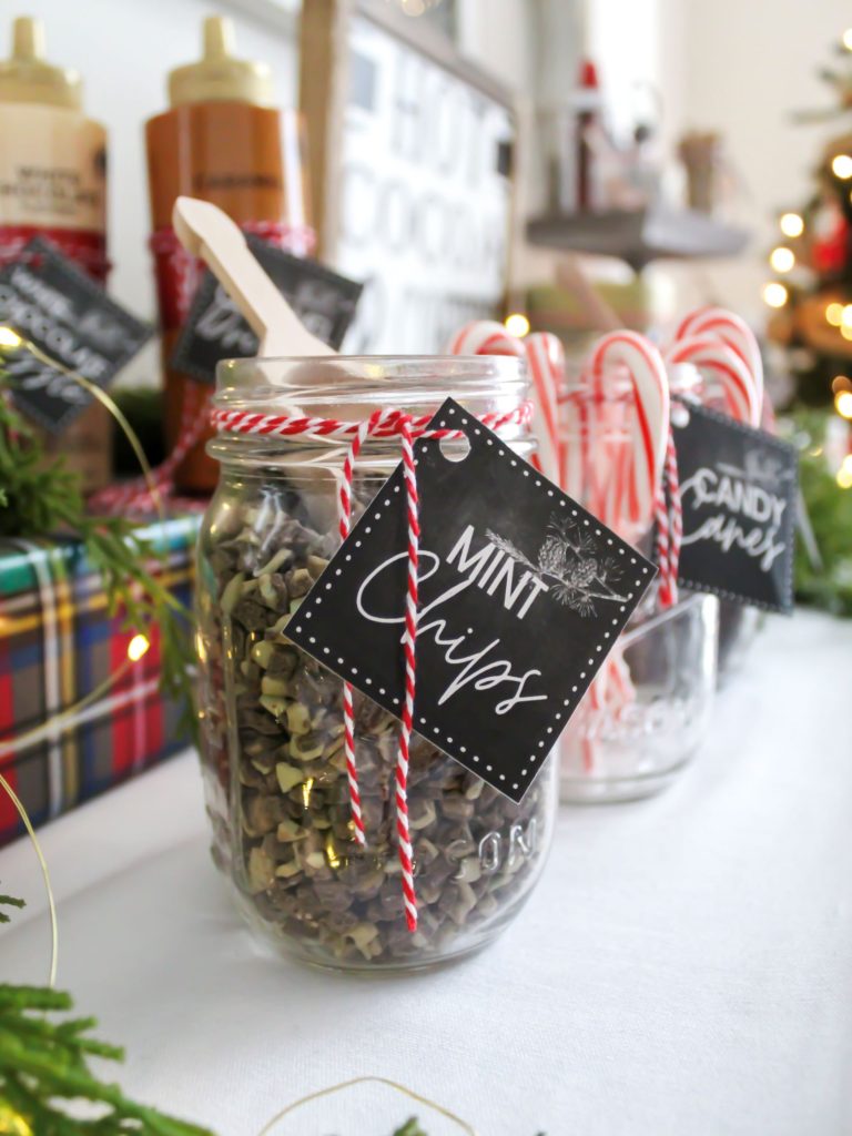 Hot cocoa bar toppings in mason jars with labels tied on with red and white holiday twine and small wood scoops