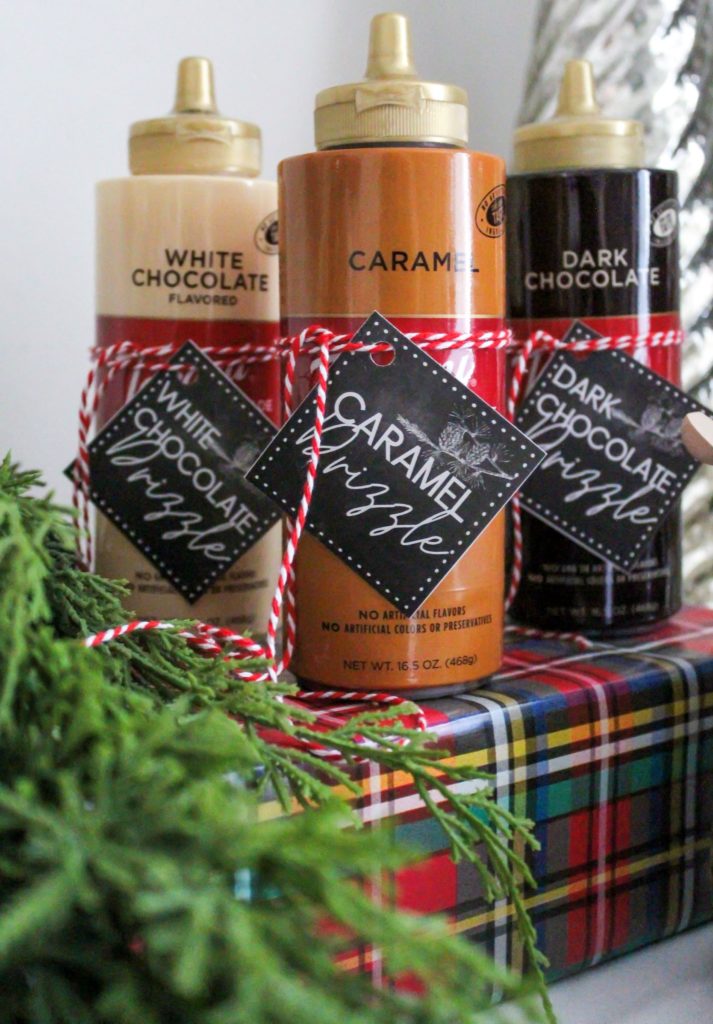 Caramel and chocolate sauce for a hot cocoa bar with labels tied on and sitting on top of a riser covered in plaid wrapping paper