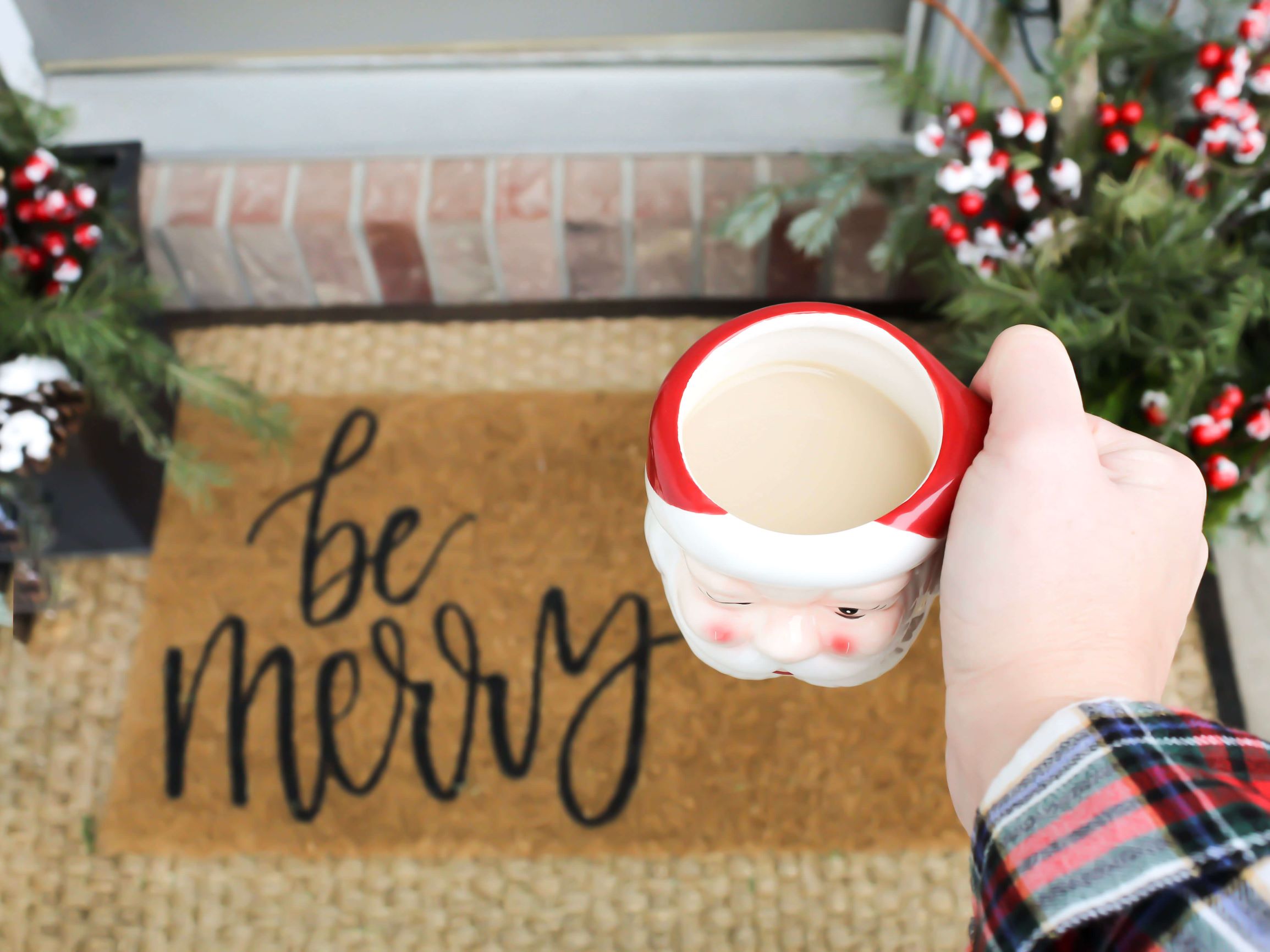 Hand cheersing with Santa Christmas mug and "be merry" Christmas door mat