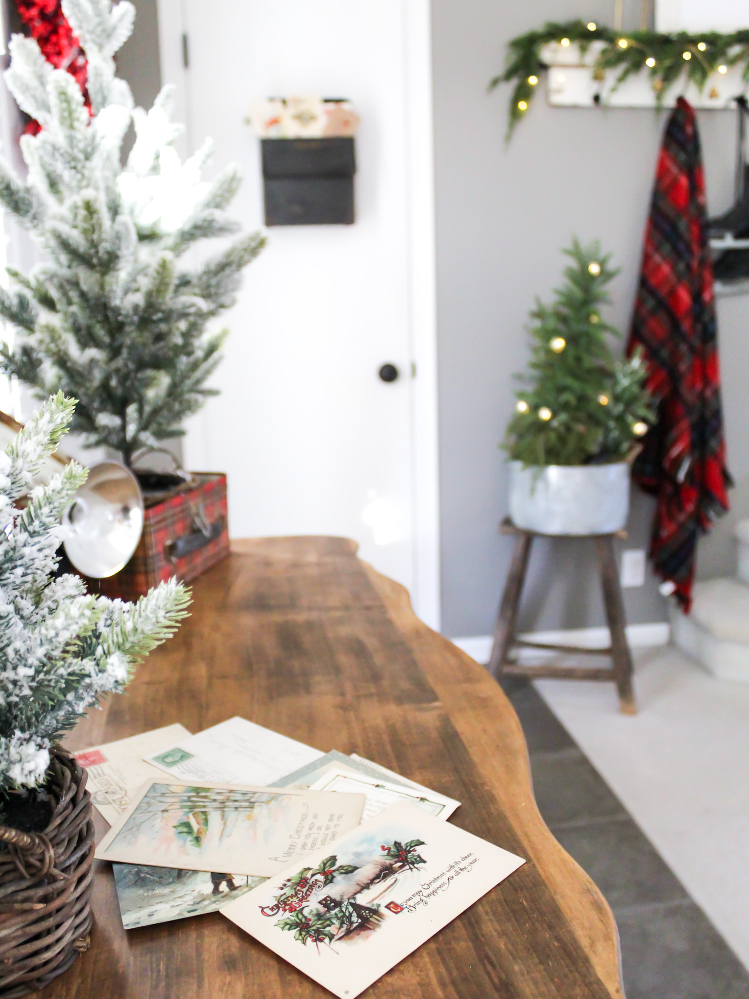 Decorating our front entry and dining room for Christmas with trees and old postcards on top of a vintage dresser with a red plaid Christmas blanket and ice skates. hanging in the background