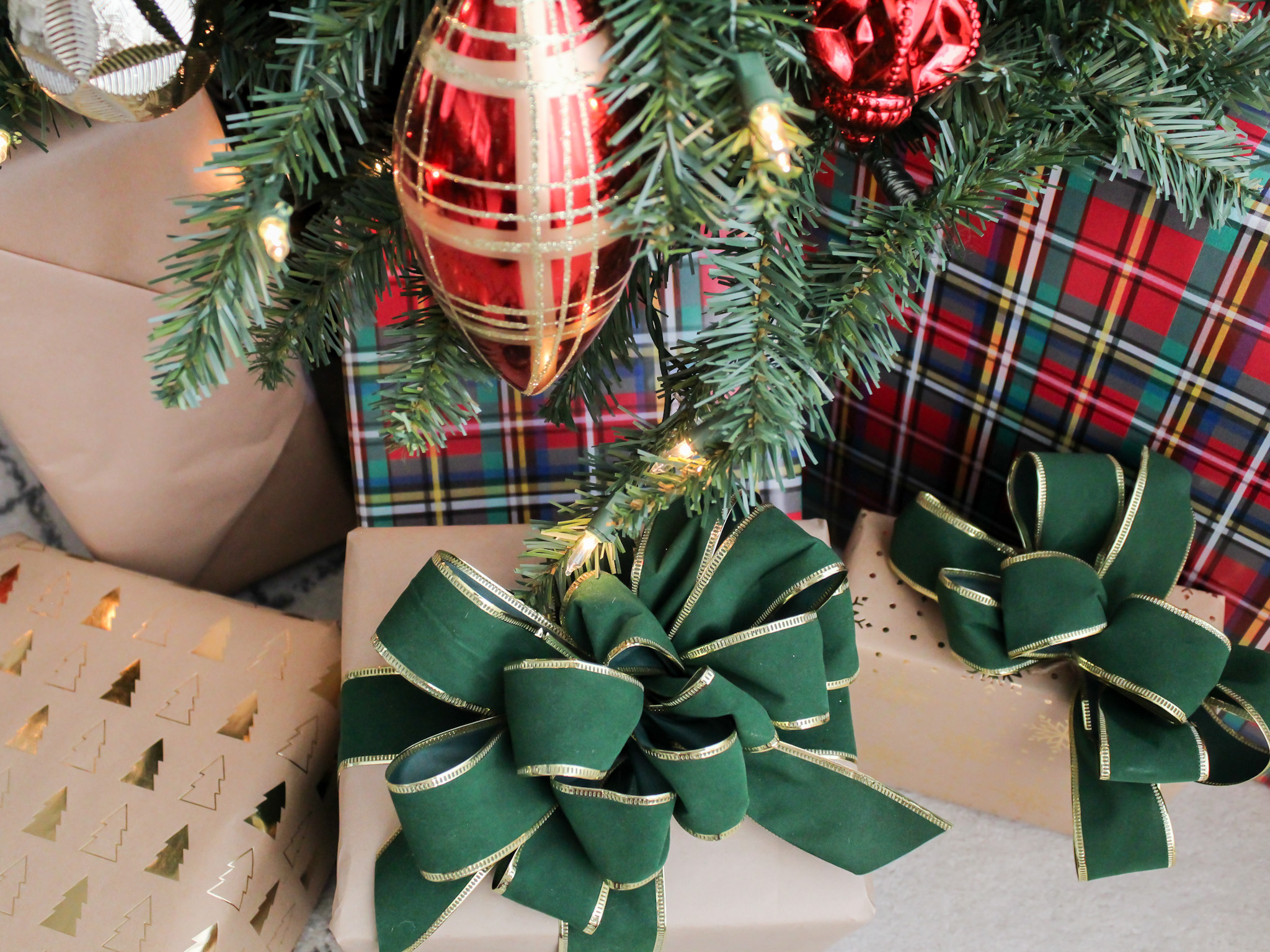 Presents under the tree with red plaid wrapping paper and green velvet bows.