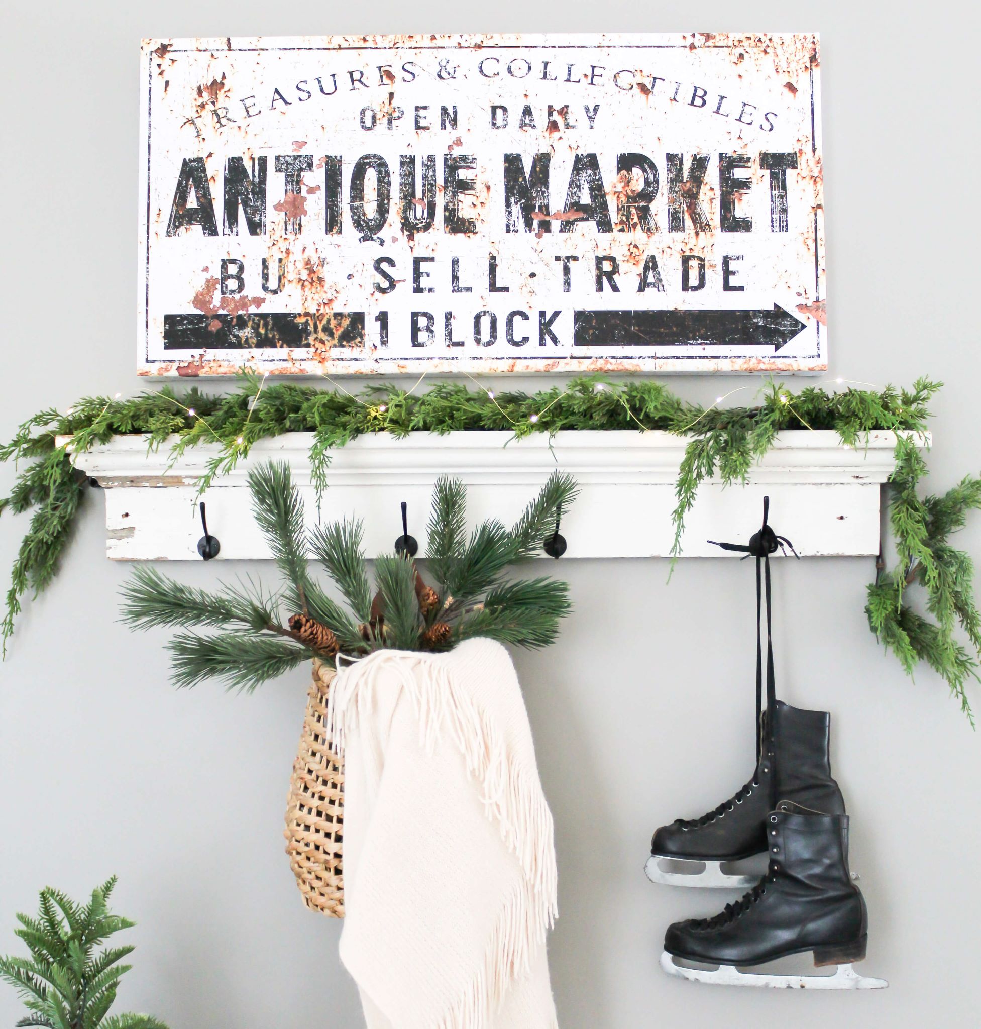 Cozy winter home wall decor with greenery, a basket with a blanket and vintage ice skates hanging from a shelf hook