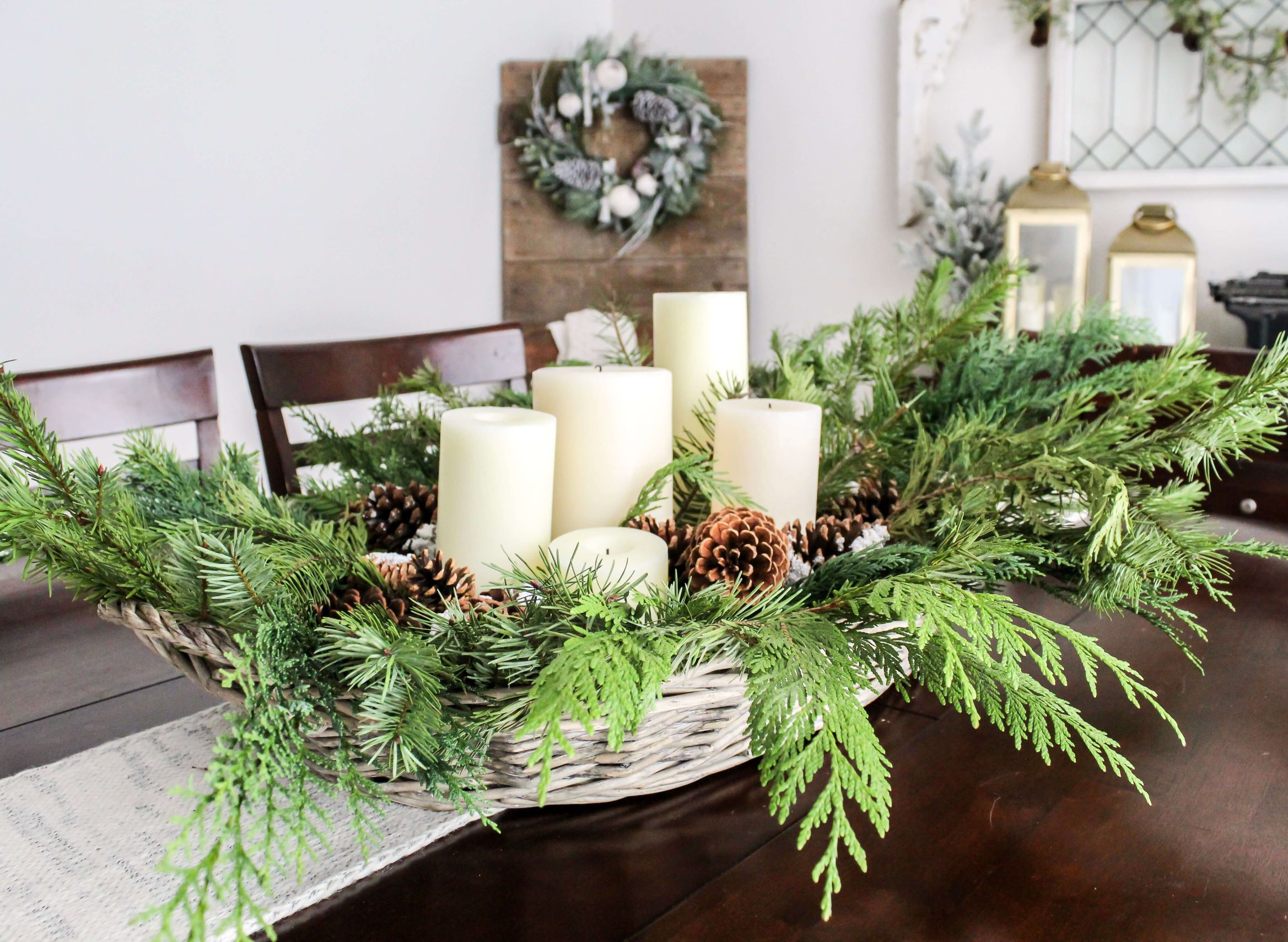 DIY centerpiece with fresh greenery, pinecones, and candles arranged in a basket and styled on a dining room table