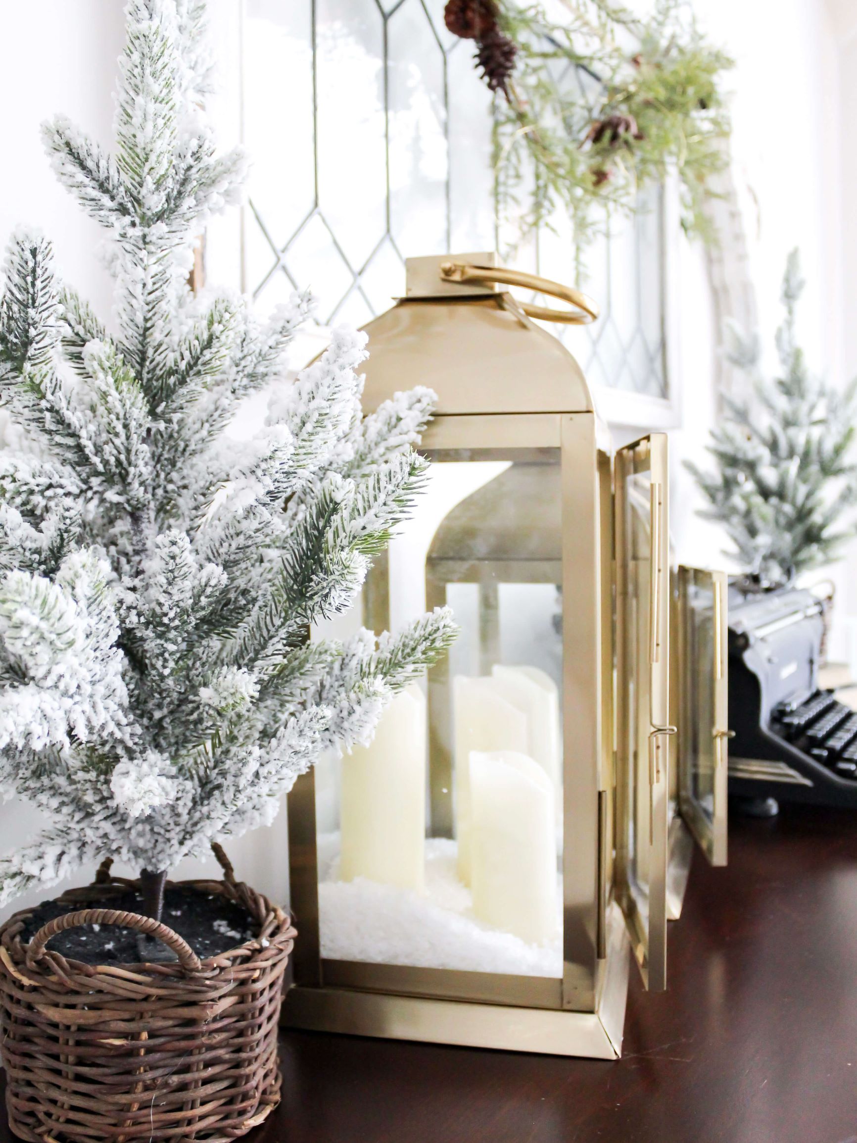 A neutral winter vignette styled on a buffet table with gold lanterns and mini flocked trees in a basket