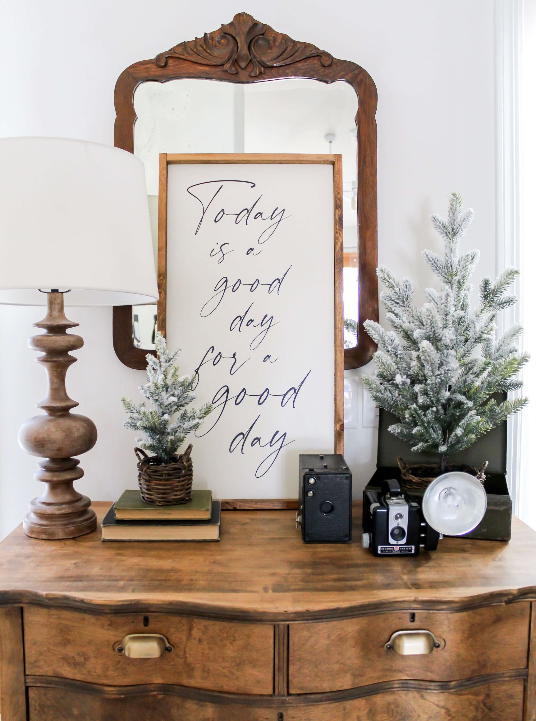 Vintage dresser in the entry styled for winter with a cozy scene including a wooden sign, antique cameras, and small flocked treese in baskets