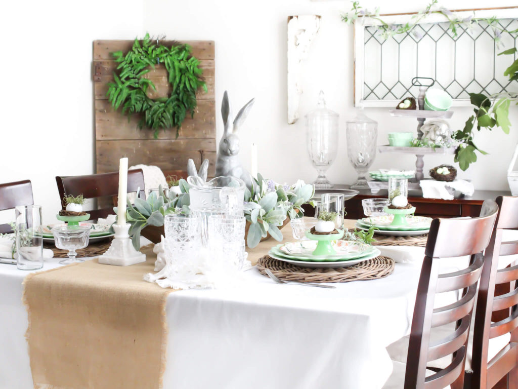 View of a dining room with cottage style decor and a tablescape set for Easter with jadeite dishes and a dough bowl centerpiece with bunnies, lambs ear, and lavender