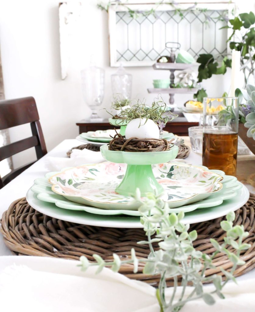 Close-up view of an Easter place setting on a tablescape with jadeite dishes, floral paper plates, and small nests with plastic eggs