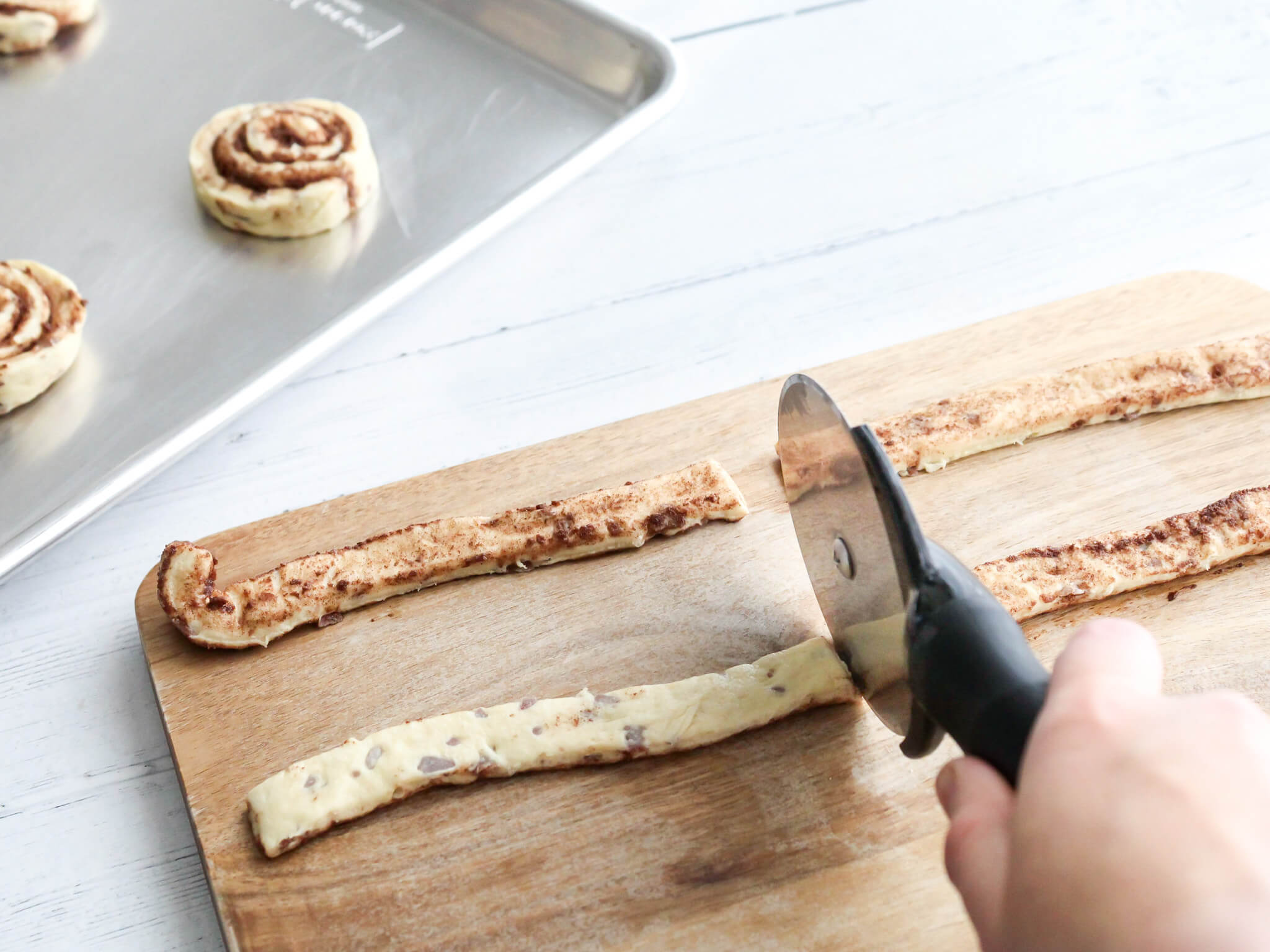 Cutting the canned cinnamon roll strips with a pizza cutter to make Easter Bunny shaped cinnamon rolls