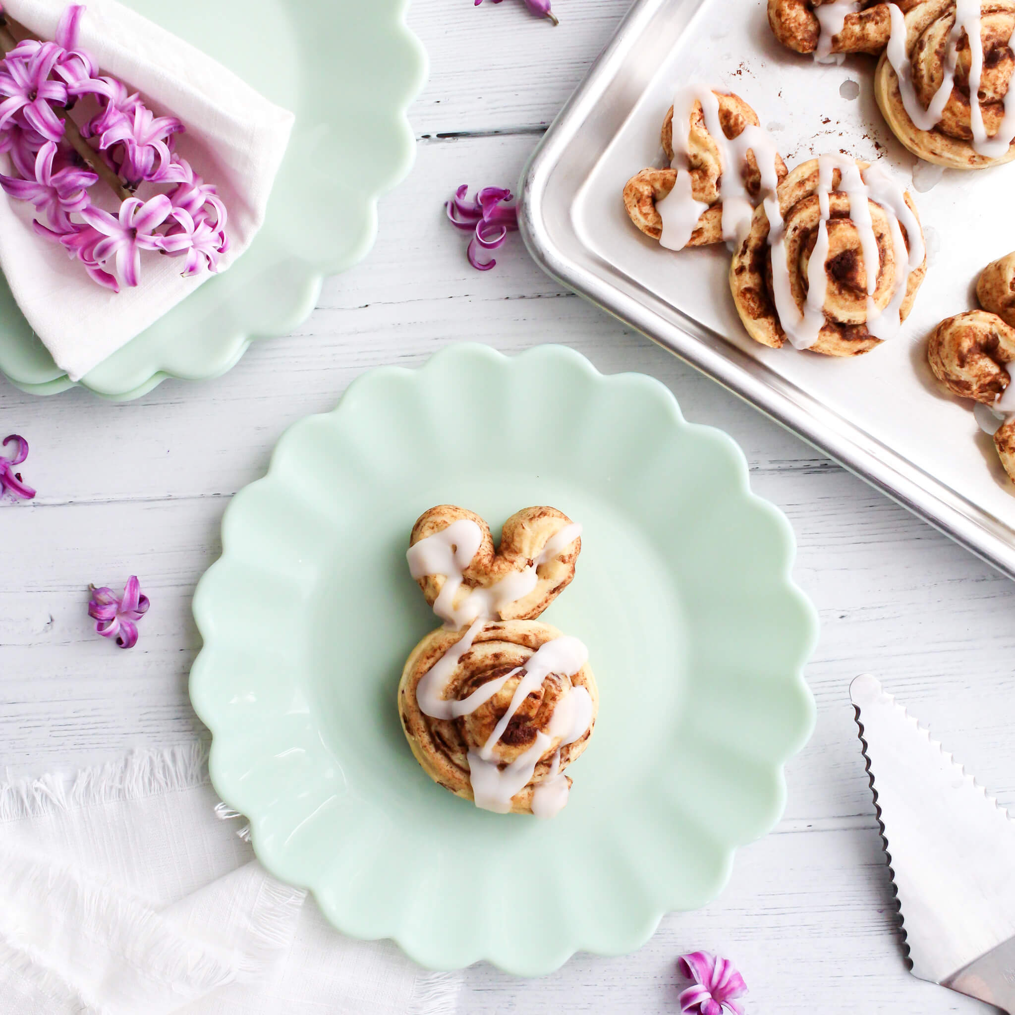 Overhead view of Easter Bunny Cinnamon Rolls on a baking sheet and one plated up on a jadeite plate