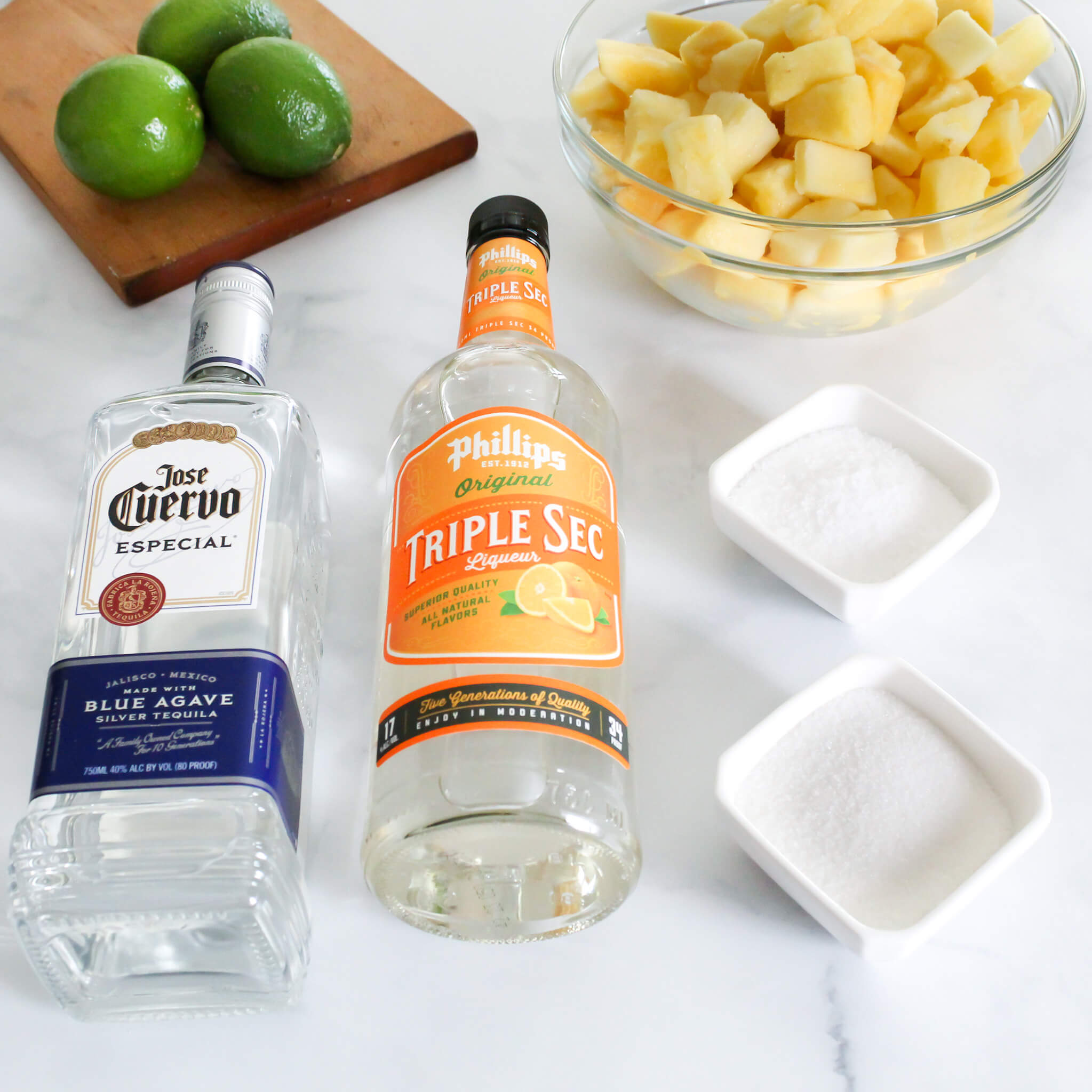 Ingredients to make a frozen pinapple margarita including tequila, limes, pineapple, triple sec and sugar. 