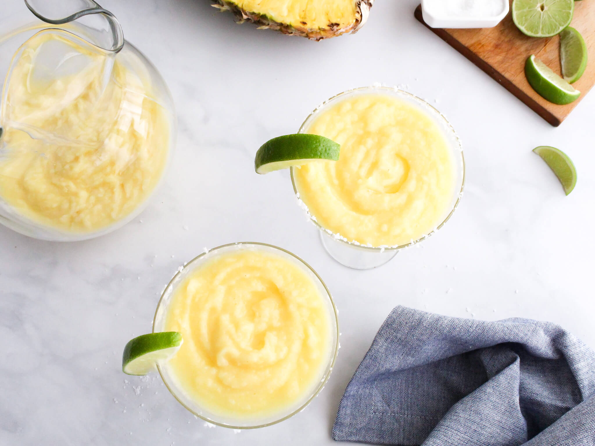 Frozen Pineapple Margarita served up in two margarita glasses and garnished with slices of limes