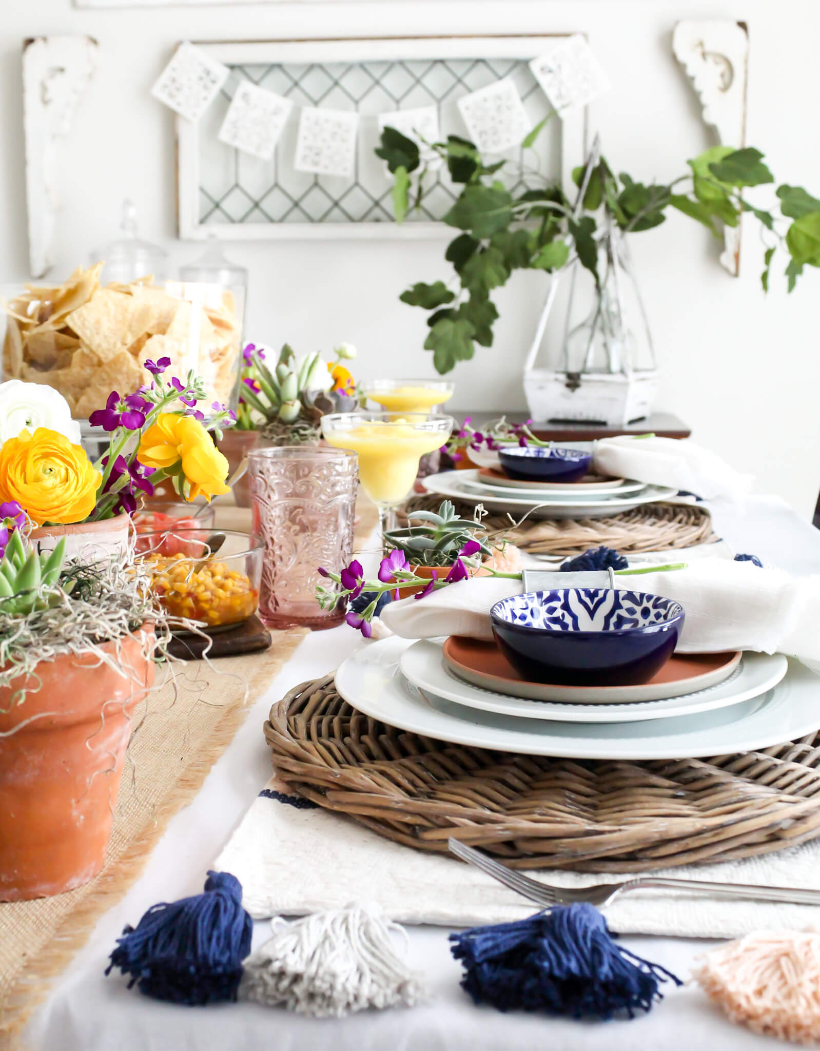 Dining room table set for a festive Cinco de Mayo party with colorful floral centerpieces in terra cotta pots, and bright Mexican dishware