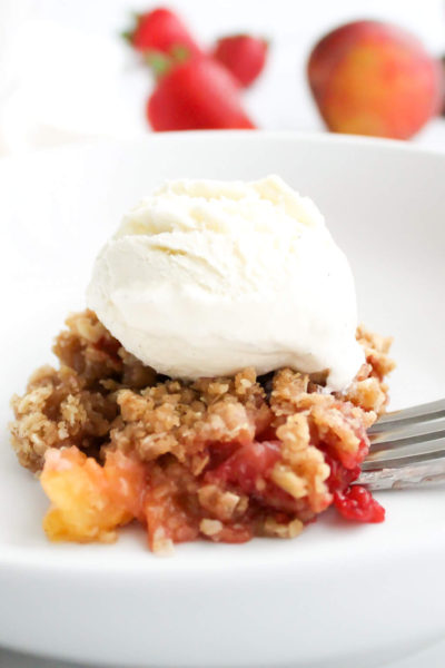 Old Fashioned Strawberry Peach Crisp Topped with Vanilla Ice Cream and a Fork with a Bite on It