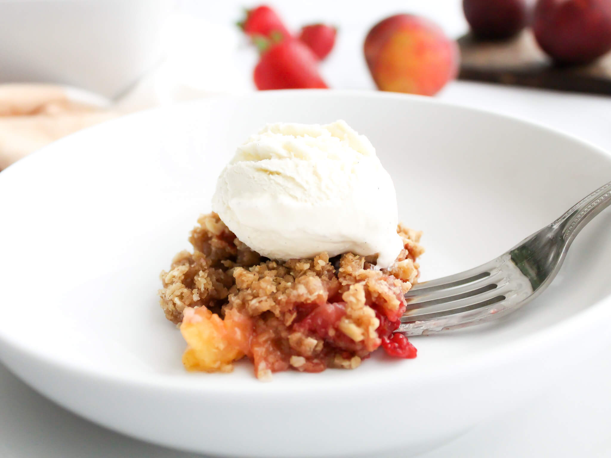 Old Fashioned Strawberry Peach Crisp Topped with Vanilla Ice Cream and a Fork with a Bite on It