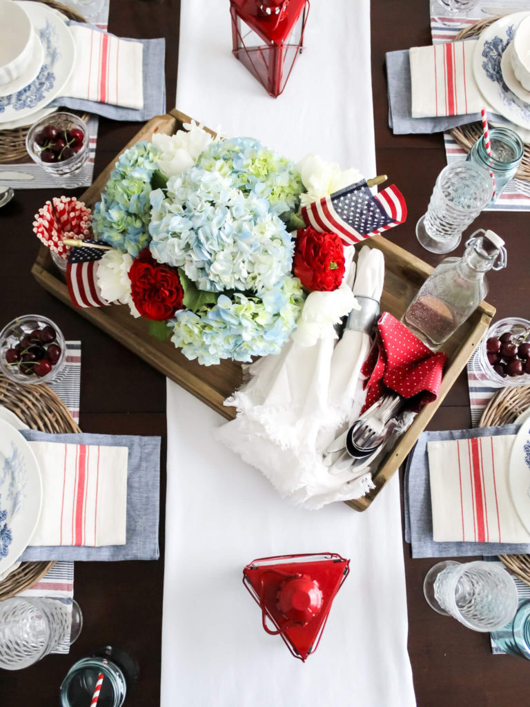 Overhead view of 4th of July red, white and blue flower centerpiece witih patriotic American flag decor displayed on the dining room table