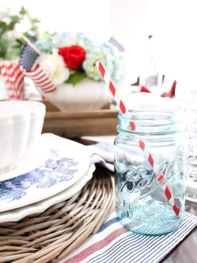 Vintage teal ball jar drinking glass with a patriotic red and white striped straw set on a Fourth of July table