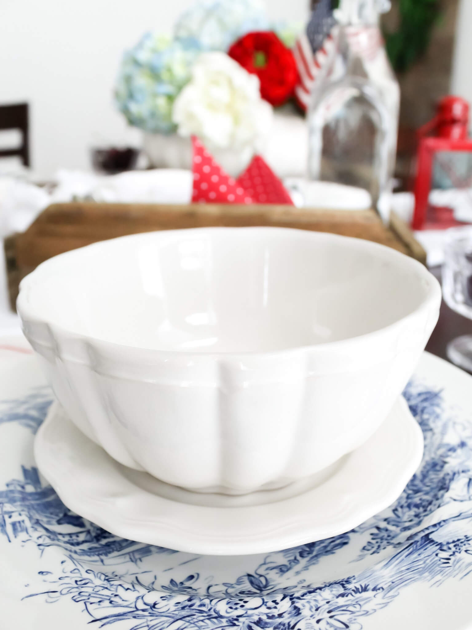 Close up view of 4th of July place setting created with patriotic decor including blue transferware plates, and white stoneware dishes