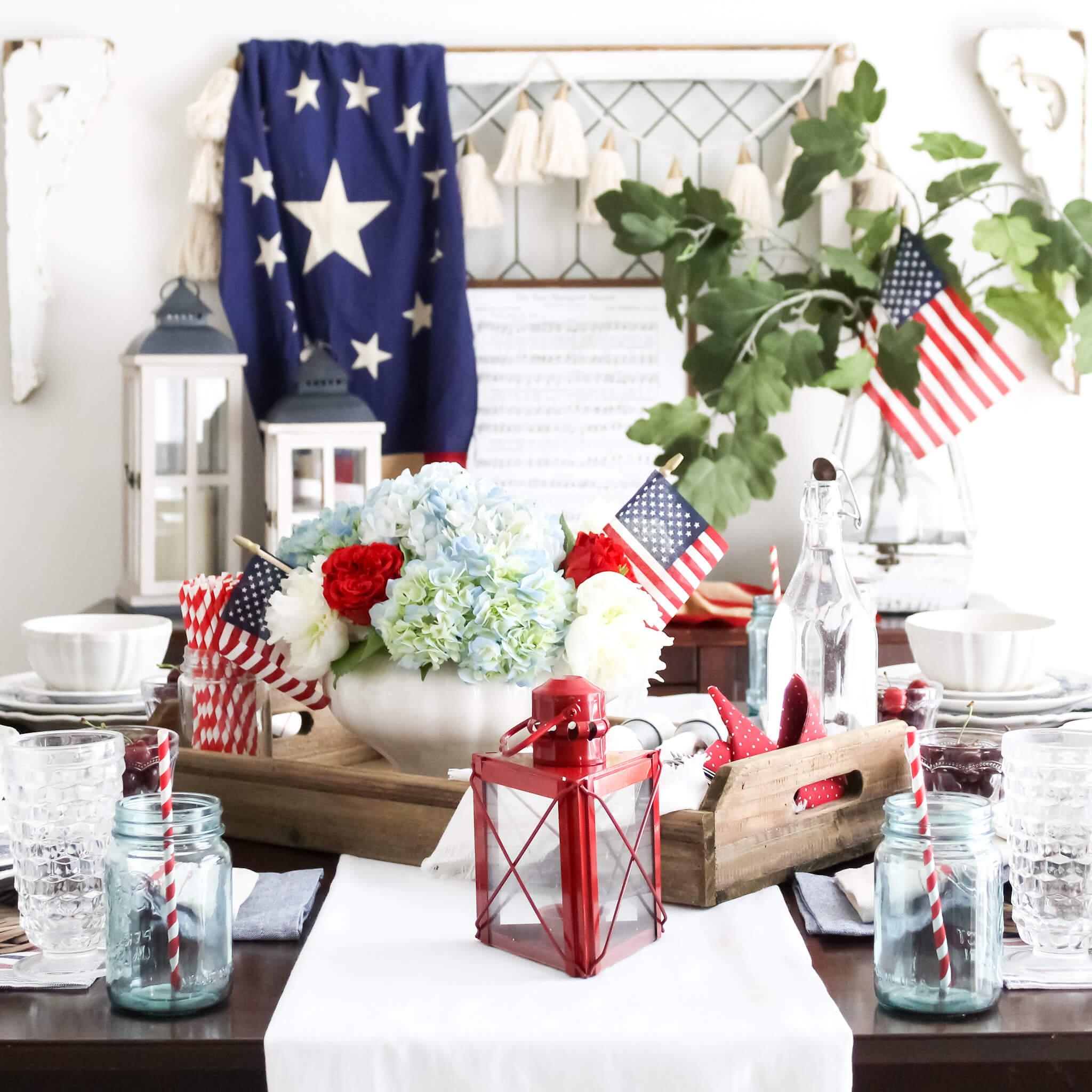 Elegant 4th of July tablescape with a red, white, and blue flower cetnerpiece set on the dining room table with a vintage American flag and patritoic decor styled on the buffet in the background