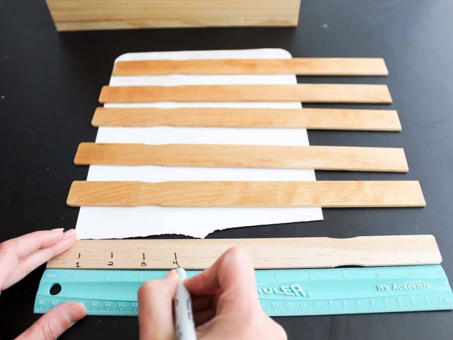 Using a marker to make the paint stir sticks look like wood rulers - Midwest Life and Style Blog