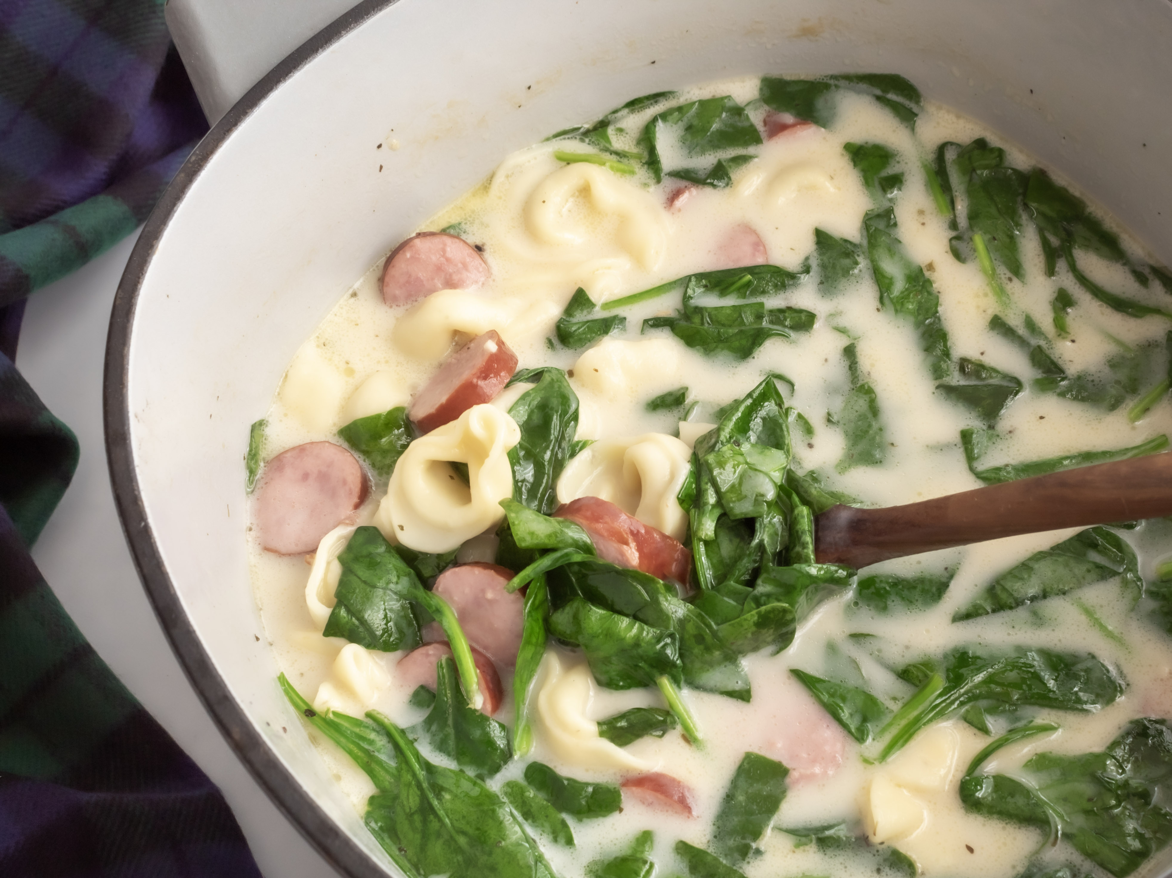 Up close view of creamy tortellin soup with kielbasa and spinach in a large Dutch oven.