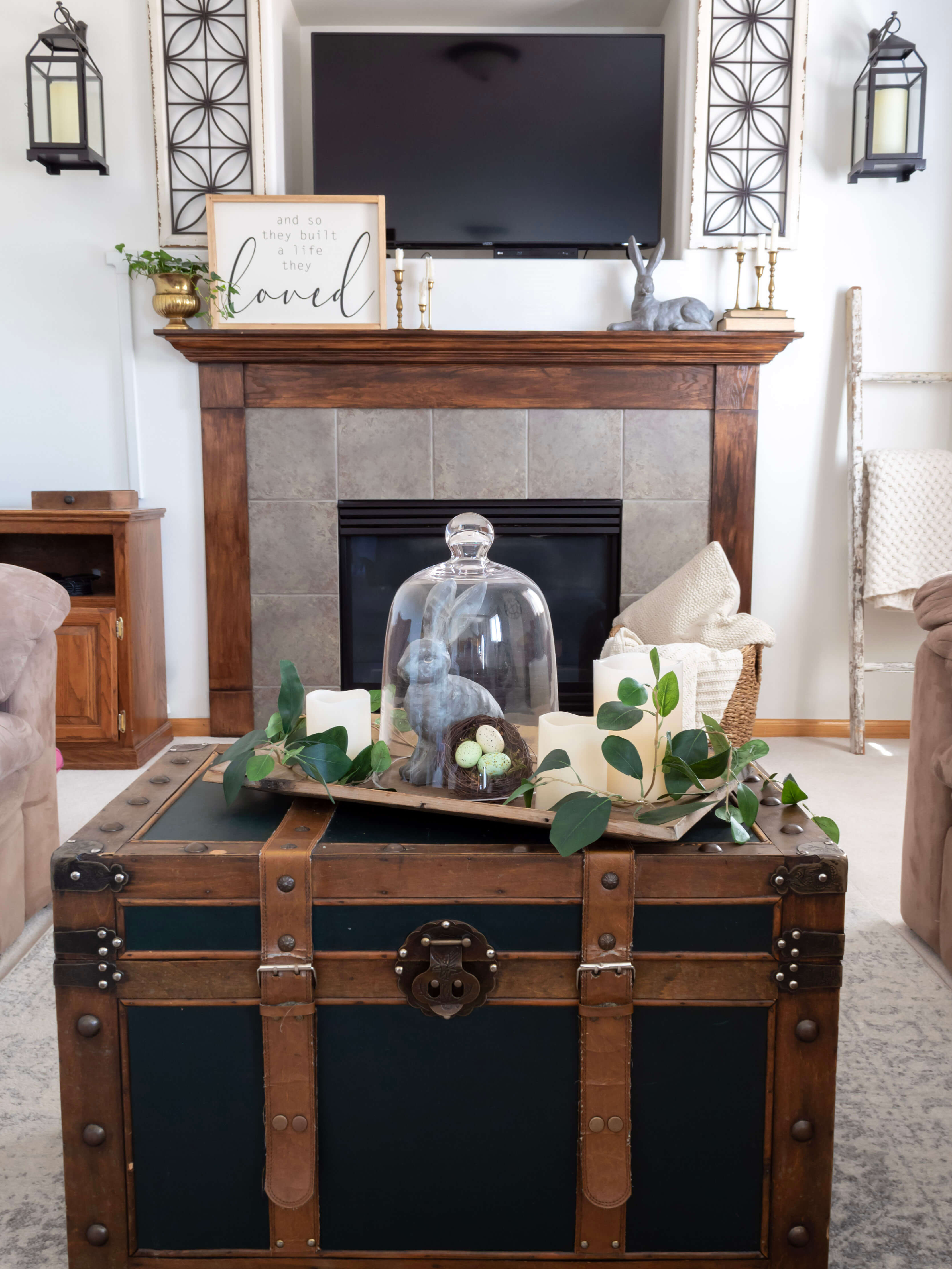 View of living room with chest coffee table and fireplace mantel decorated for spring with bunnies and greenery