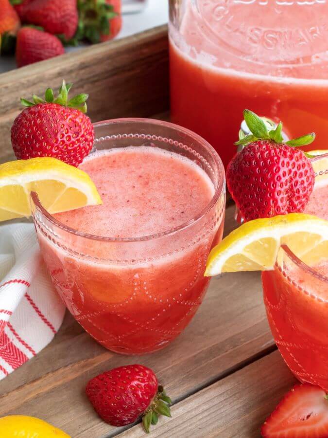 Glasses of Spiked Strawberry Lemonade with Gallon Pitcher in the Background 