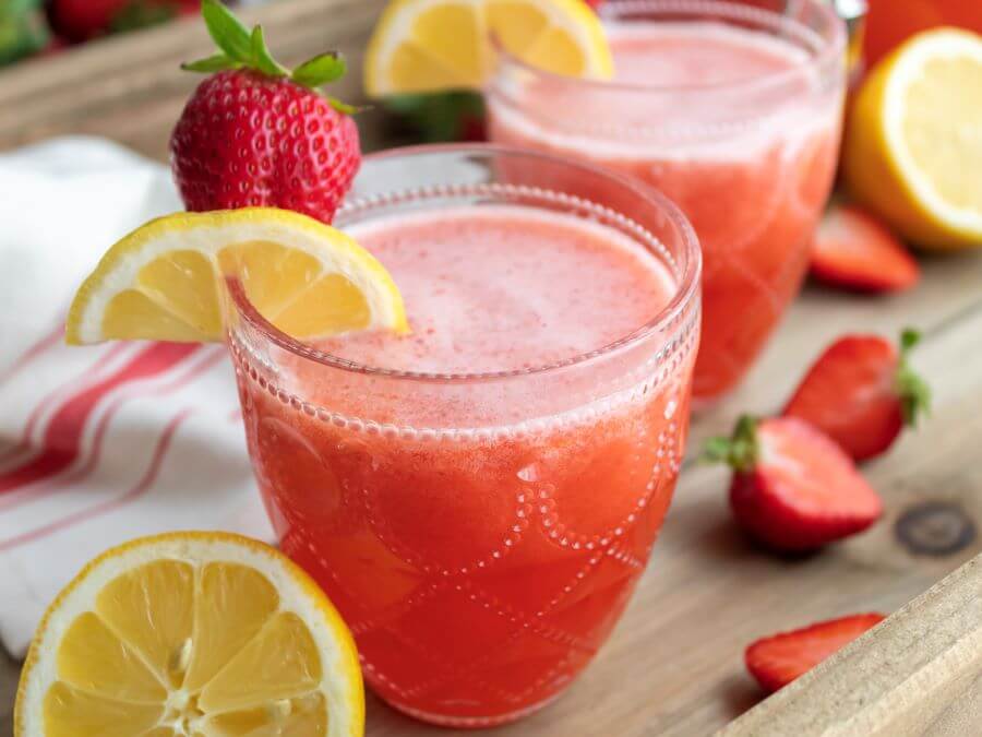 Glasses of Spiked Strawberry Lemonade Garnished with a Lemon Wedge and Fresh Strawberies