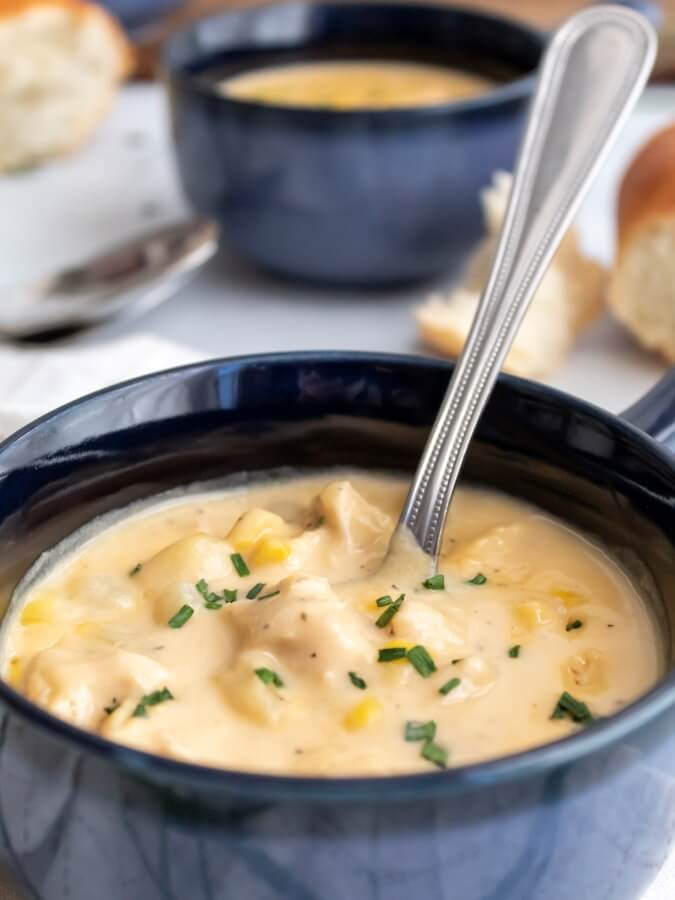 Creamy chicken and corn chowder in a bowl with a spoon with another bowl and crusty french bread in the background