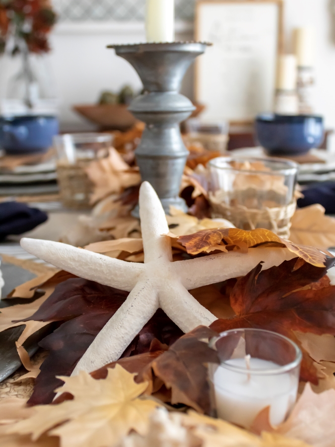 Close up view of fall leaf and seashell garland centerpiece for a coastal table setting with starfish, tea lights and rustic metal candlesticks. 