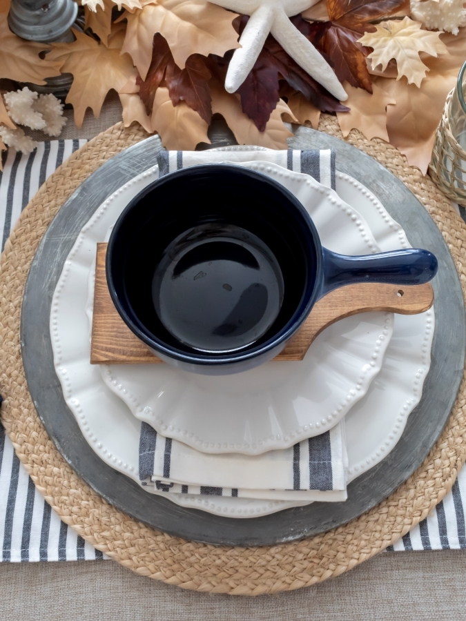 Nautical and beach placesSetting for autumn with blue bowls, white plates, striped linens, and metal and woven chargers. 