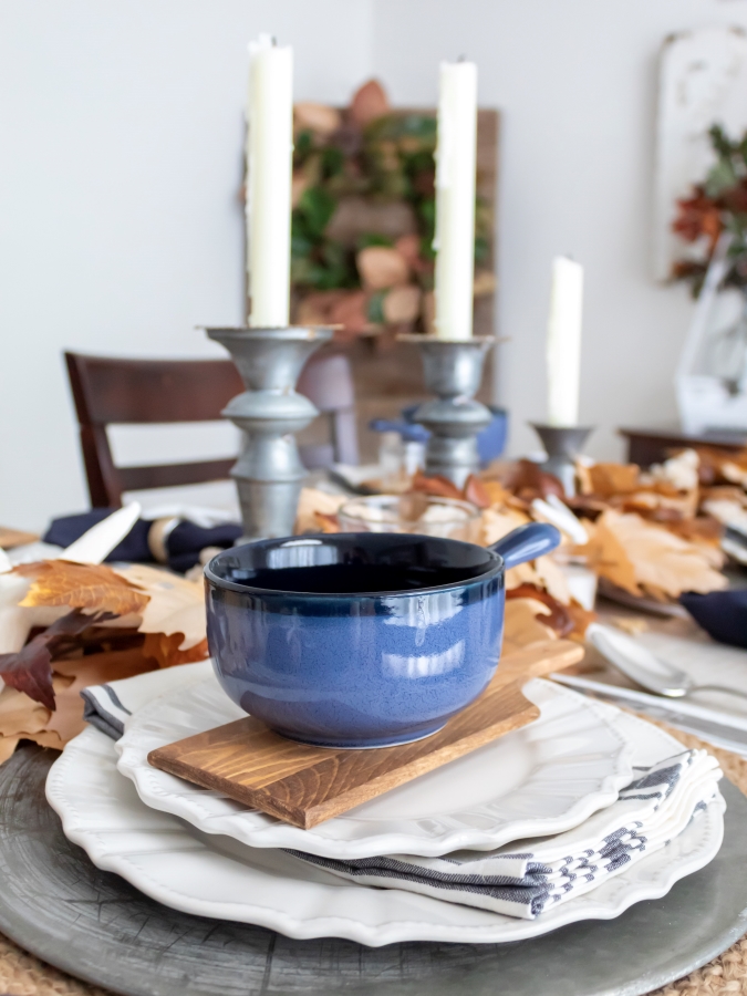 Blue soup bowls on a small bread board with with with white dishes for a coastal fall place setting in a dining room decorated for fall