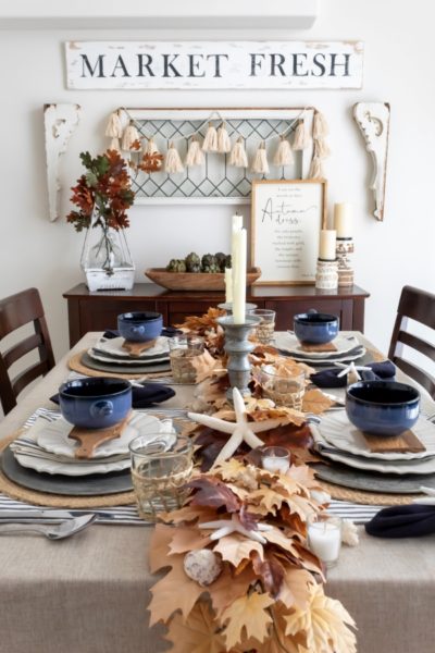 Coastal fall tablescape styled on a dining talbe with a leaf and sea shell garland centerpiece and fall decor styled on the buffet in the background