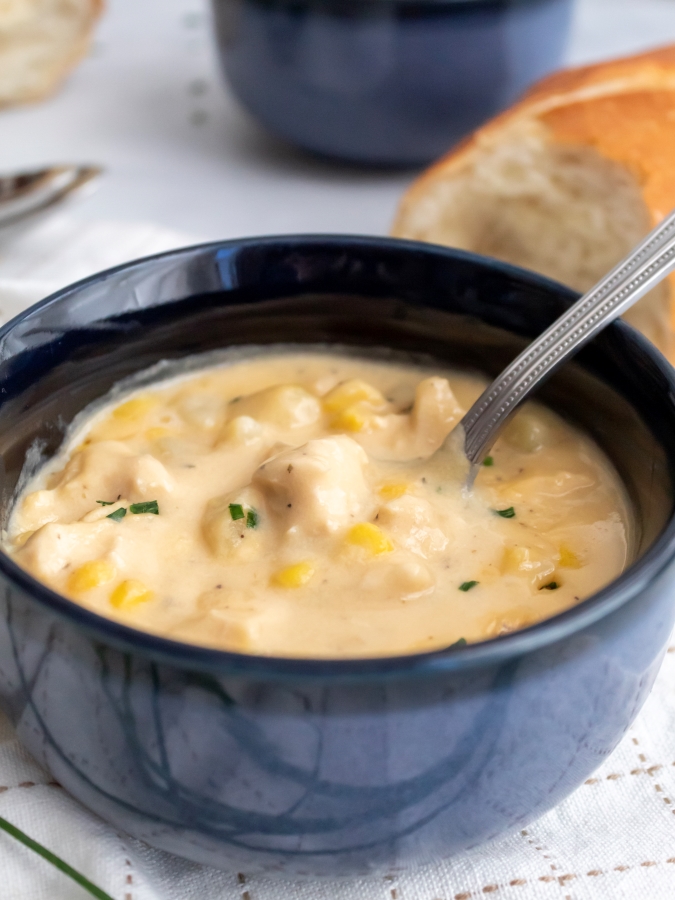 Creamy Chicken and Corn Chowder served in a blu soup bowl with a spoon and french bread on the side