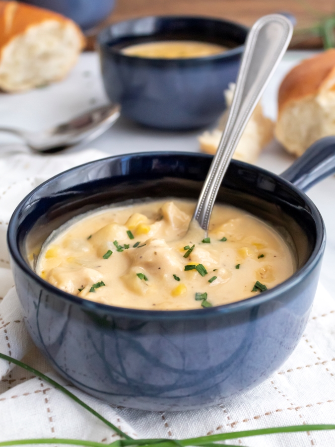 Bowl of Creamy Chicken and Corn Chowder with a second bowl and french bread seen in the background