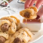 Breakfast sausage crescent rolls sprinkled with everything bagel seasoning being dipped in maple syrup