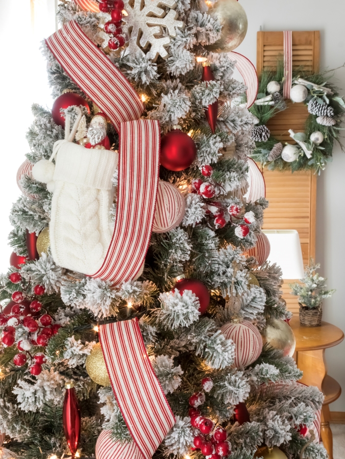 Side view of flocked Christmas tree decorated with white and red ornaments and ticking stripe ribbon