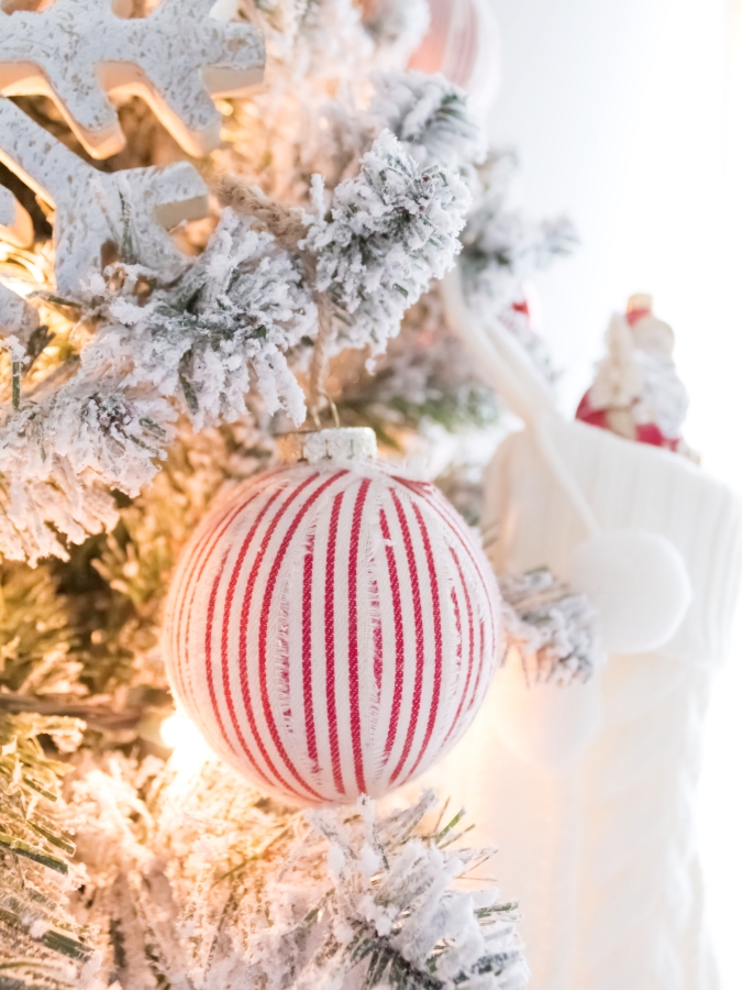 Decorating a flocked Christmas tree with white and red ornaments and red and white ticking stripe Christmas balls