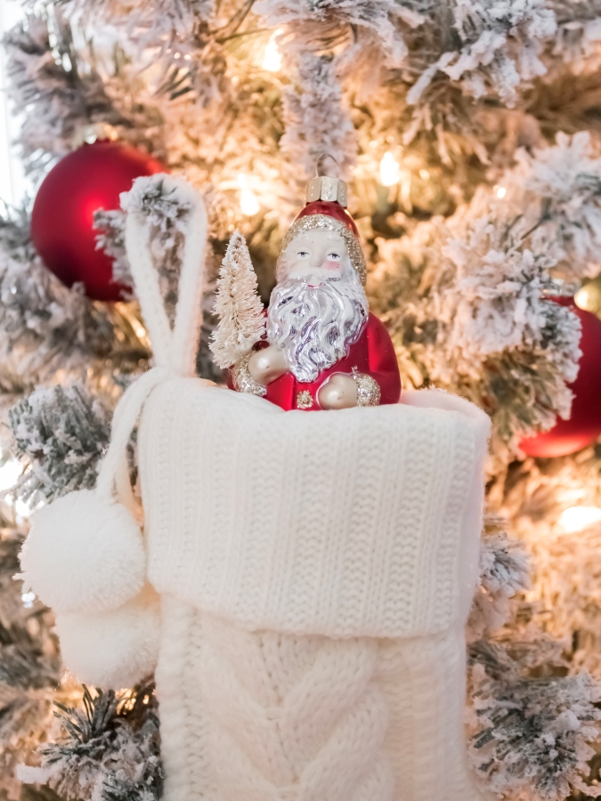 Vintage looking Santa ornament nestled in a mini Christmas stocking hanging on a flocked Christmas tree