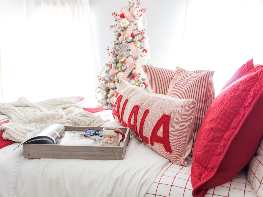 Christmas bedding with red and white flannel sheets, red shams, red and white ticking stripe throw pillows and and a decorated flocked tree in teh background