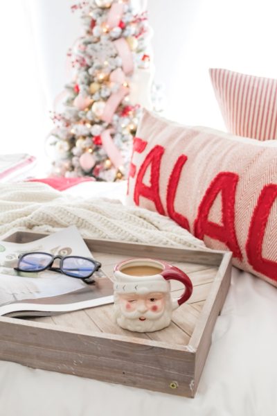 Bedroom decorated for Christmas with red and white decorations, Christmas bedding, and breakfast tray on the bed with a santa mug filled with coffee