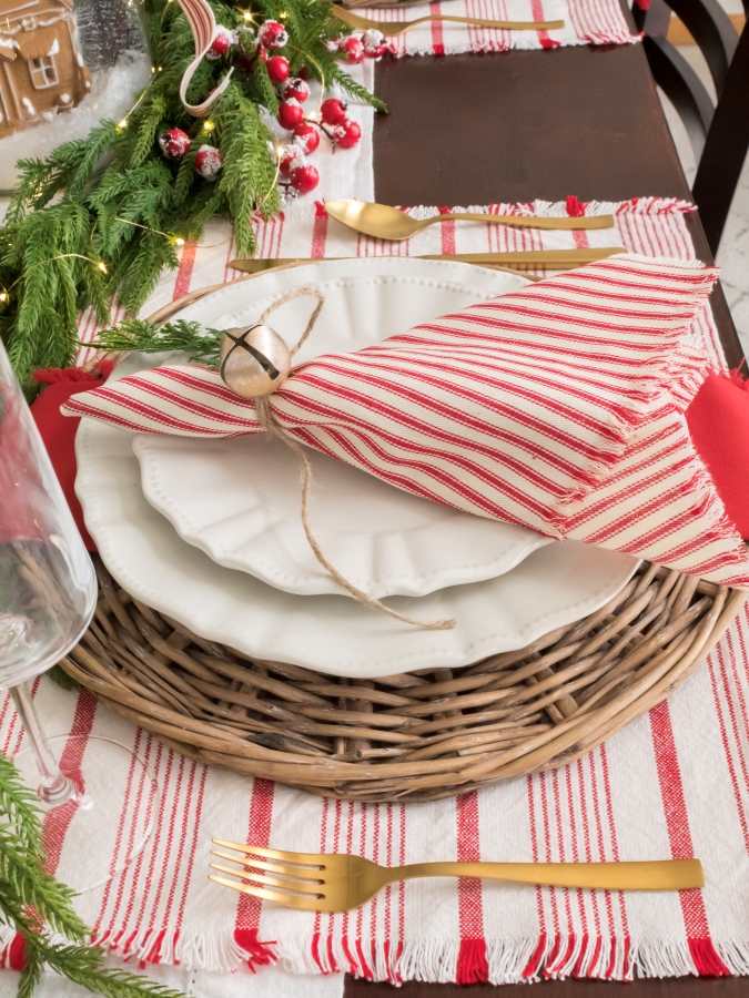 Red and white ticking stripe napkins with bell tied, white dishes, and gold silverware on a Christmas tablescape 