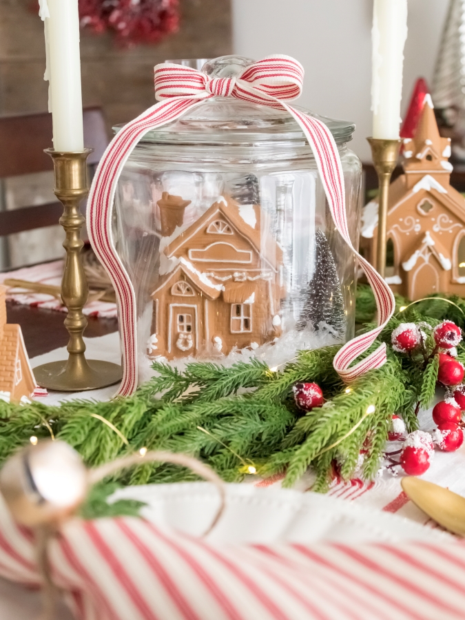 Upcycled Christmass village house painted to look like a gingerbread house in a glass jar with bottle brush trees to make a DIY snow globe centerpiece