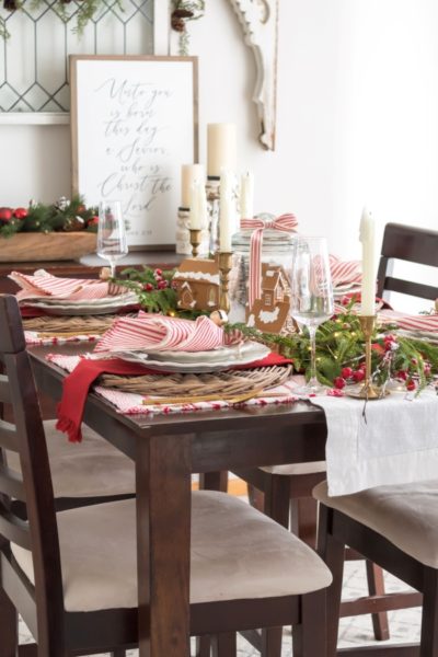 Red and white gingerbread Christmas tablescapewith ticking stripe napkins, garland, vintage brass candlesticks and a DIY gingerbread snowglobe centerpiece