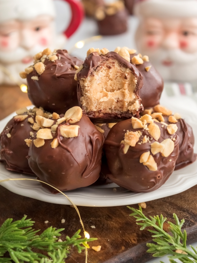 Chocolate Covered Peanut Butter Balls on a plate with a bite taken out of one of the PB balls with santa mugs in the background